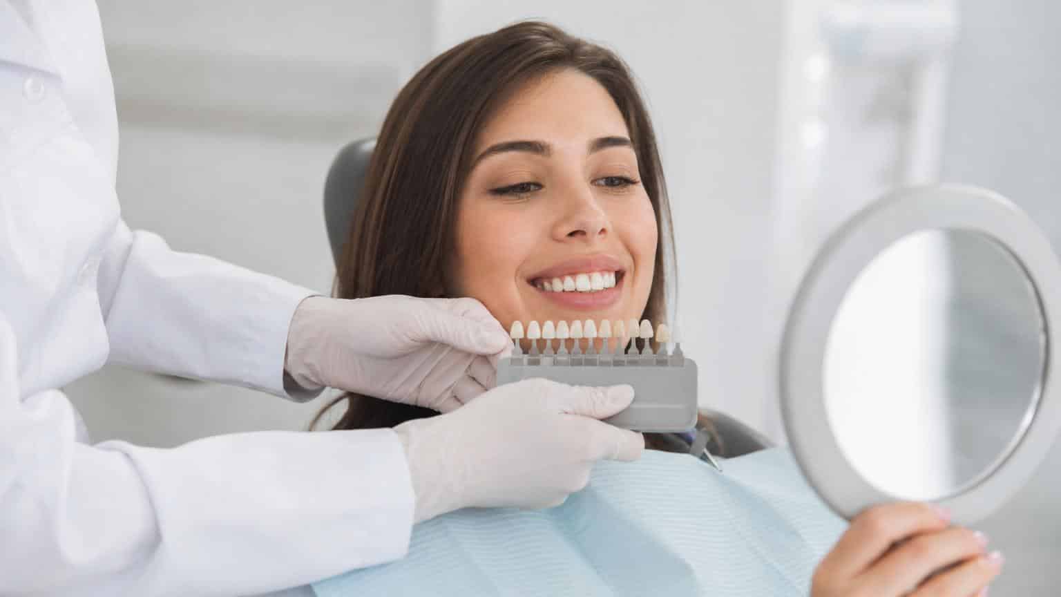 Dentist holding a tooth shade guide against a smiling woman's teeth to select the perfect color for ceramic veneers.