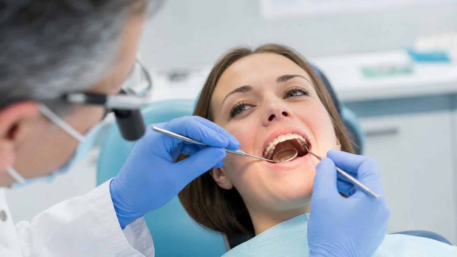 Dentist using a mirror and probe to examine lingual brackets attached to the inner surface of a patient’s teeth. Dentist using a mirror and probe to examine lingual brackets attached to the inner surface of a patient's teeth.