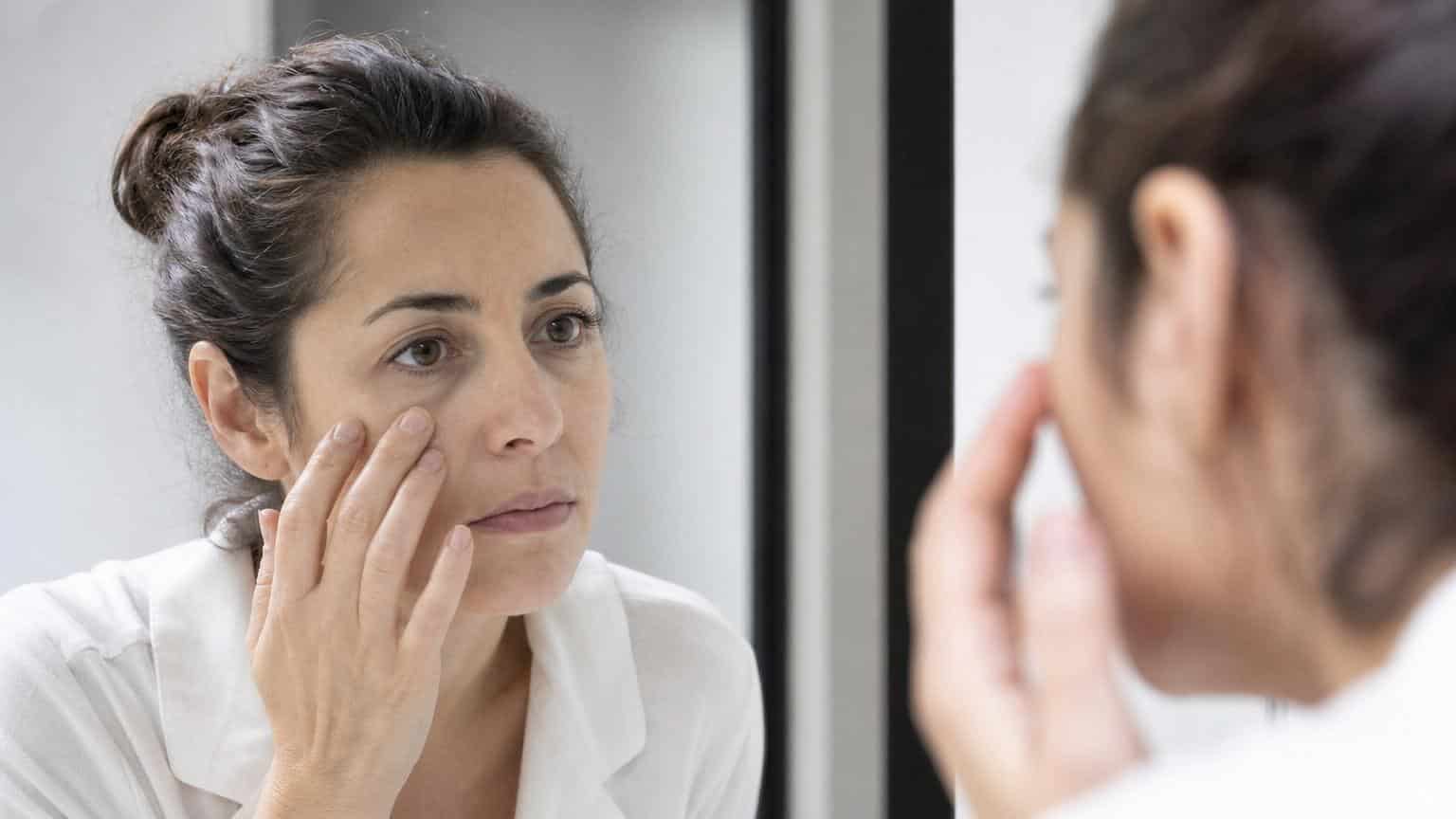 Woman looking in a bathroom mirror while touching the deep bags and dark circles under her eyes. Woman looking in a bathroom mirror while touching the deep bags and dark circles under her eyes.